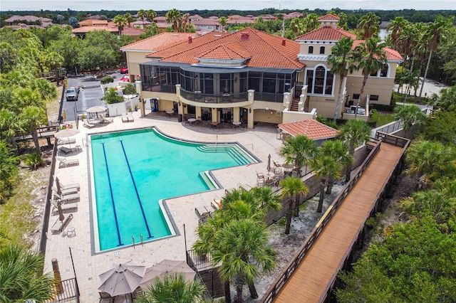 community pool with a sunroom, fence, and a patio area