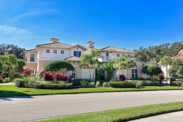 mediterranean / spanish home featuring a tile roof, a front lawn, and stucco siding