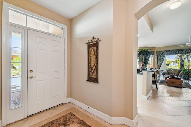 entryway featuring arched walkways, light tile patterned floors, a ceiling fan, and baseboards