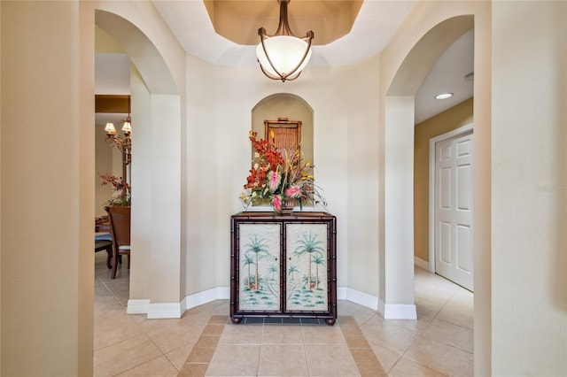 corridor with light tile patterned floors, baseboards, and arched walkways