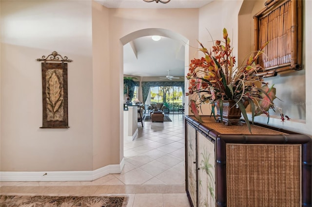 corridor featuring light tile patterned flooring, arched walkways, and baseboards