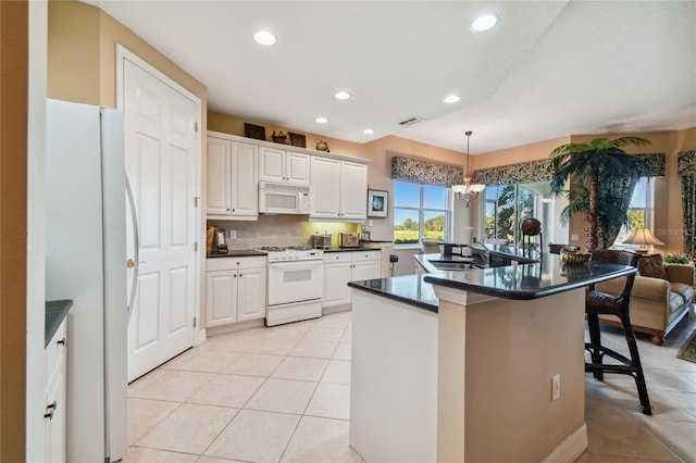 kitchen with white appliances, a breakfast bar, light tile patterned flooring, a sink, and dark countertops