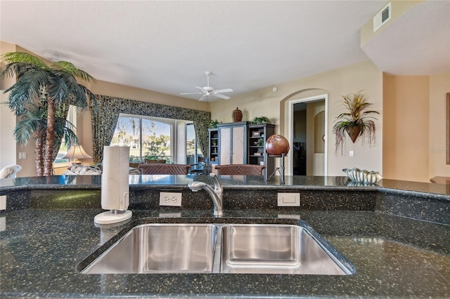 kitchen featuring a sink, visible vents, ceiling fan, and dark stone counters