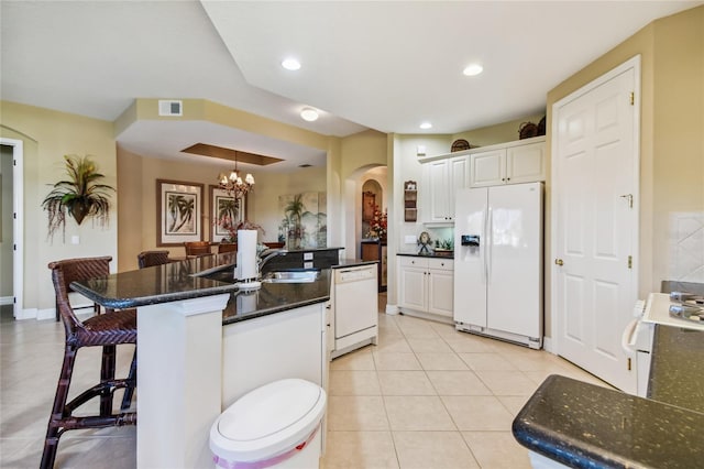 kitchen featuring visible vents, a kitchen bar, light tile patterned floors, white appliances, and a sink