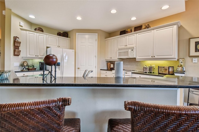 kitchen featuring a breakfast bar, decorative backsplash, dark stone countertops, white appliances, and white cabinetry