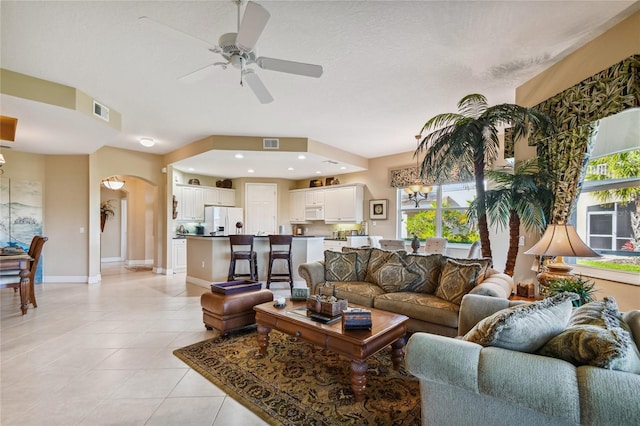 living room with light tile patterned floors, visible vents, baseboards, arched walkways, and ceiling fan with notable chandelier