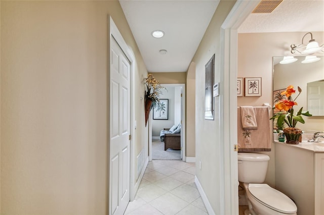 corridor with light tile patterned floors, visible vents, baseboards, and a sink