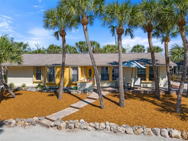 ranch-style house featuring roof with shingles and stucco siding