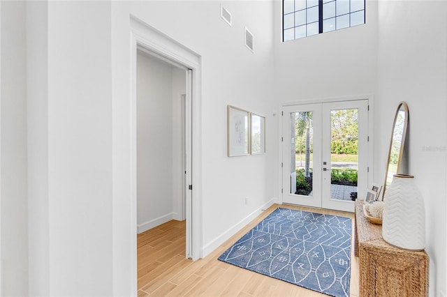 entrance foyer featuring visible vents, baseboards, a towering ceiling, wood finished floors, and french doors