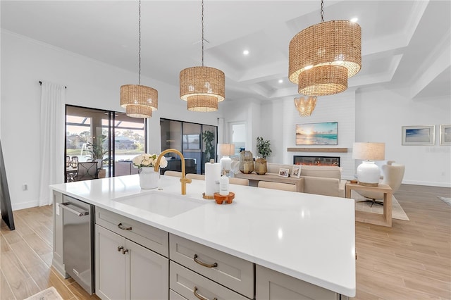 kitchen with light wood-style floors, a glass covered fireplace, light countertops, and a sink