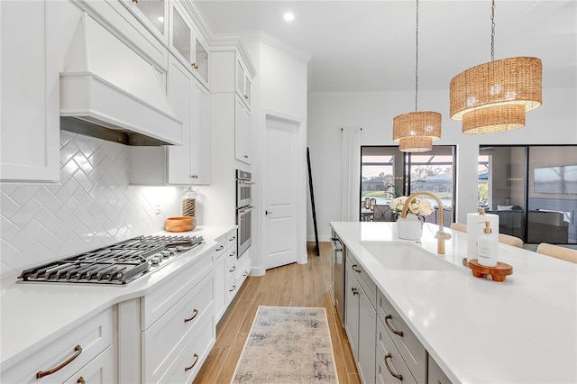 kitchen featuring light wood finished floors, custom exhaust hood, light countertops, appliances with stainless steel finishes, and a sink