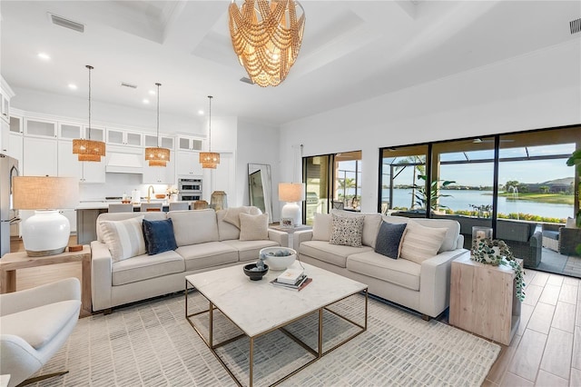 living room featuring a water view, coffered ceiling, visible vents, and light wood-style floors