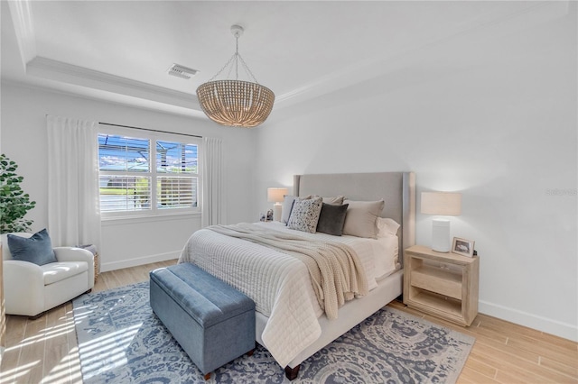 bedroom with a notable chandelier, wood finished floors, a raised ceiling, and baseboards