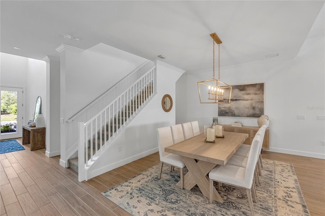 dining space featuring crown molding, light wood finished floors, stairway, an inviting chandelier, and baseboards