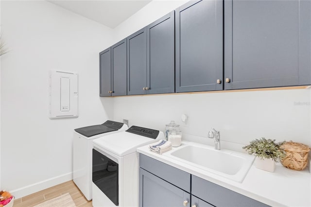 clothes washing area with cabinet space, light wood-style flooring, washing machine and dryer, a sink, and baseboards