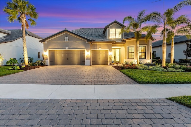 view of front of house with decorative driveway, a tile roof, an attached garage, and stucco siding