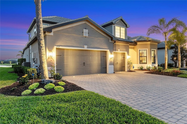 view of front of property with a garage, cooling unit, decorative driveway, and stucco siding