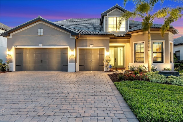 view of front of house featuring a garage, a tile roof, decorative driveway, and stucco siding