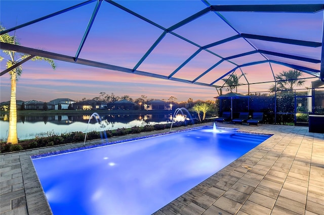 pool at dusk featuring glass enclosure, a patio, and a water view