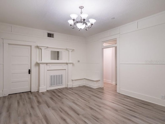 unfurnished living room featuring a notable chandelier, a textured ceiling, visible vents, and light wood-style floors