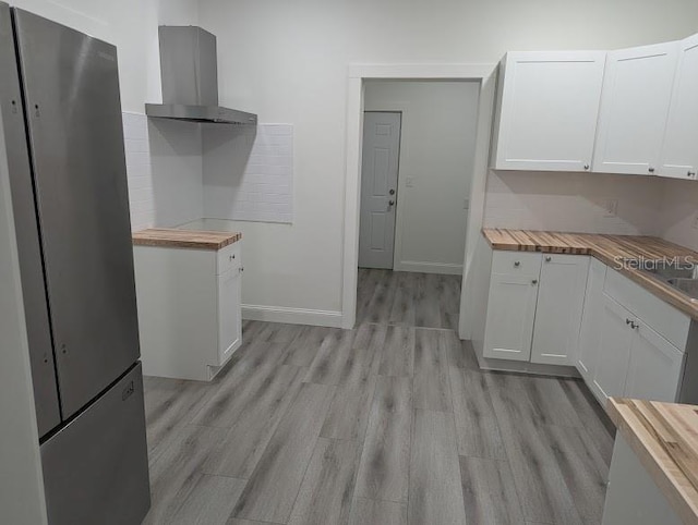 kitchen with light wood-style flooring, freestanding refrigerator, white cabinetry, butcher block countertops, and extractor fan