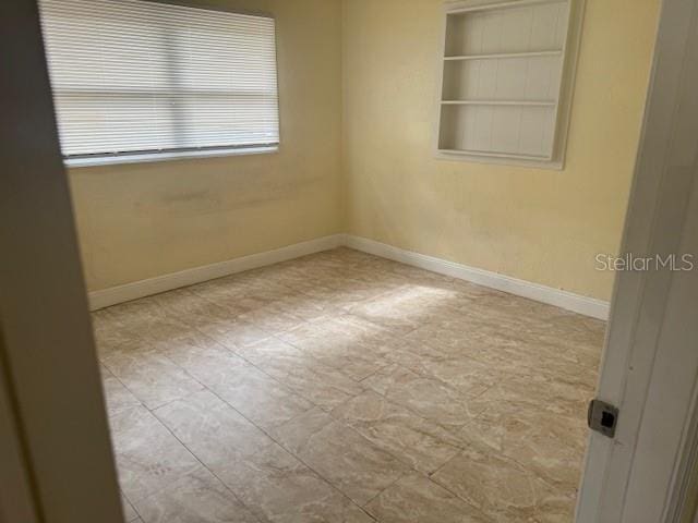 empty room with built in shelves and baseboards