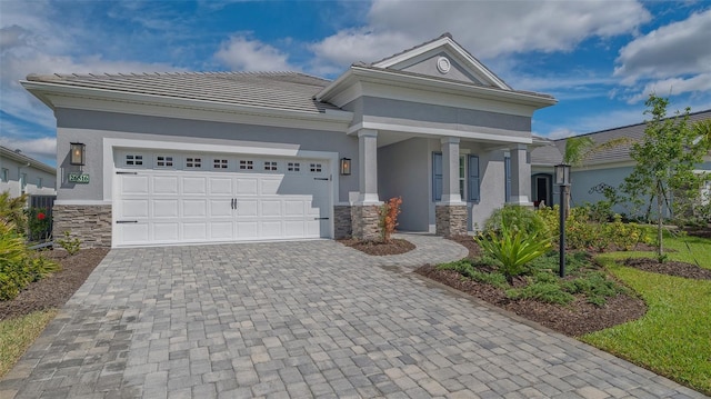 neoclassical home featuring stone siding, decorative driveway, an attached garage, and stucco siding