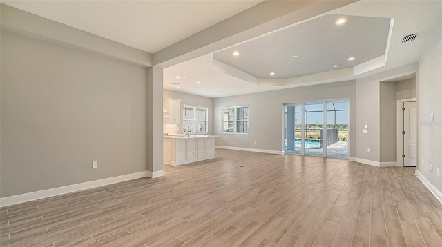 empty room featuring recessed lighting, a raised ceiling, visible vents, light wood-style floors, and baseboards