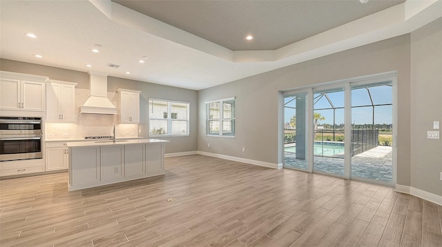 kitchen featuring light wood finished floors, custom exhaust hood, tasteful backsplash, light countertops, and baseboards