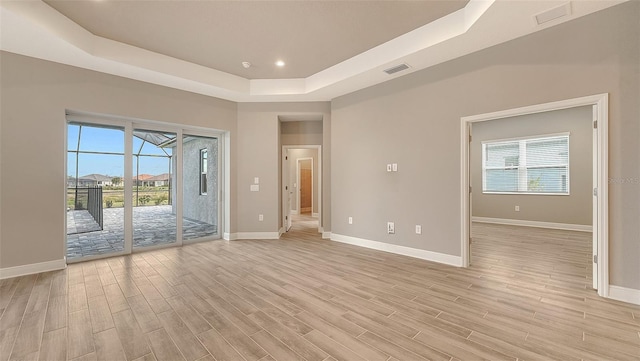 unfurnished room featuring light wood finished floors, baseboards, visible vents, a tray ceiling, and recessed lighting