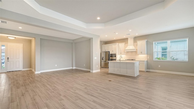 kitchen featuring custom range hood, appliances with stainless steel finishes, open floor plan, a kitchen island with sink, and a sink