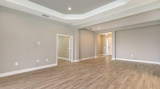 unfurnished room featuring light wood finished floors, recessed lighting, a raised ceiling, visible vents, and baseboards