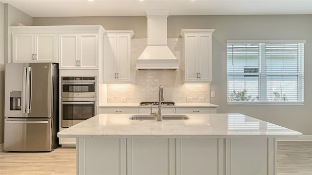 kitchen featuring custom exhaust hood, tasteful backsplash, appliances with stainless steel finishes, white cabinets, and light wood-type flooring