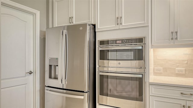 kitchen with white cabinets, light stone countertops, appliances with stainless steel finishes, and decorative backsplash