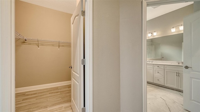 interior space with wood finished floors, a sink, baseboards, a spacious closet, and double vanity