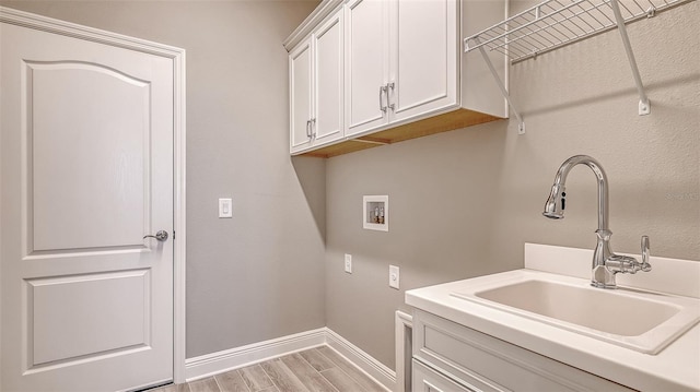 laundry area with washer hookup, light wood finished floors, cabinet space, a sink, and baseboards