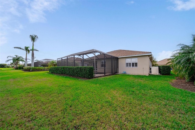 back of house with a tile roof, glass enclosure, a lawn, and stucco siding