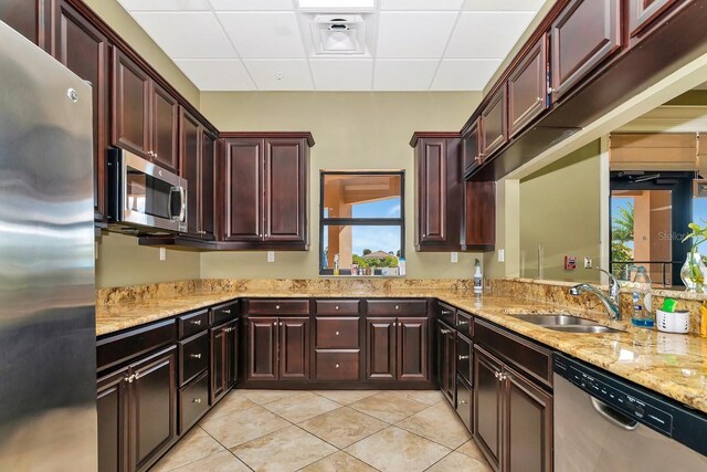 kitchen with appliances with stainless steel finishes, light tile patterned flooring, a sink, and light stone countertops