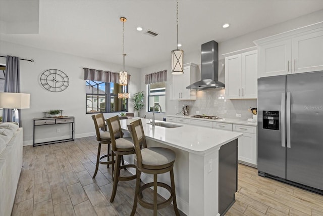 kitchen with tasteful backsplash, light countertops, appliances with stainless steel finishes, a sink, and wall chimney exhaust hood