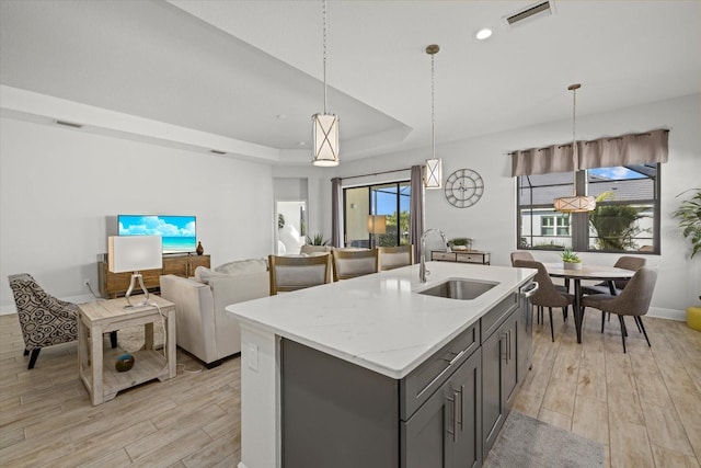 kitchen with a tray ceiling, a sink, visible vents, and light wood-style floors