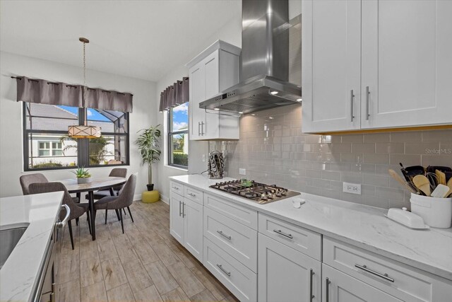 kitchen featuring white cabinetry, wall chimney range hood, tasteful backsplash, decorative light fixtures, and stainless steel gas stovetop