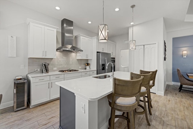 kitchen with stainless steel appliances, a sink, light countertops, wall chimney range hood, and tasteful backsplash