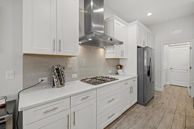 kitchen featuring decorative backsplash, wall chimney exhaust hood, stainless steel appliances, light countertops, and white cabinetry