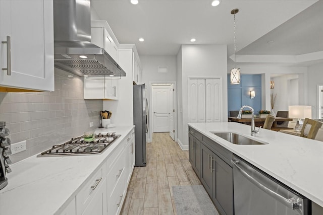 kitchen featuring stainless steel appliances, a sink, white cabinetry, wood tiled floor, and wall chimney exhaust hood