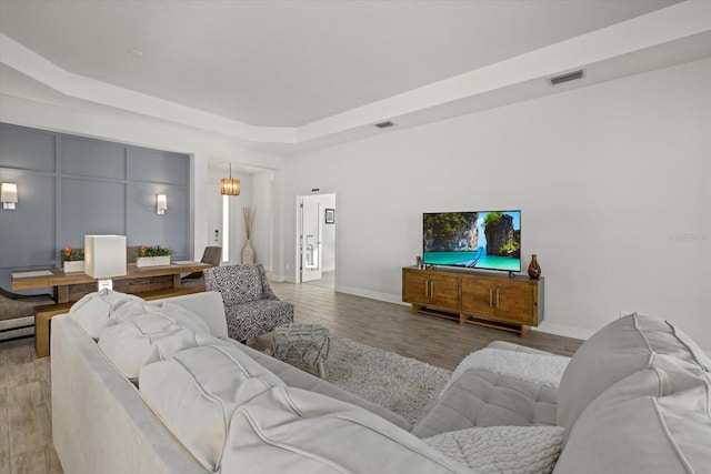 living room featuring light wood finished floors, baseboards, visible vents, and a raised ceiling