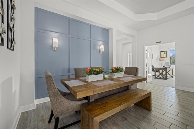 dining area featuring a raised ceiling, a decorative wall, and wood finished floors