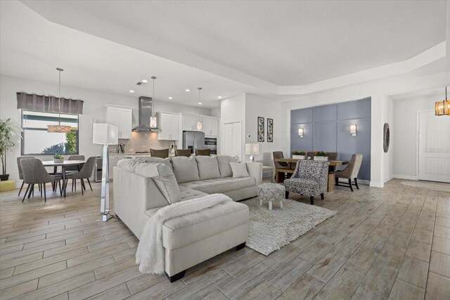 living area with wood finish floors, an inviting chandelier, a raised ceiling, and recessed lighting