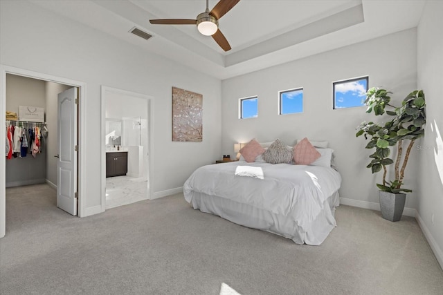 bedroom with carpet floors, visible vents, baseboards, a tray ceiling, and a walk in closet