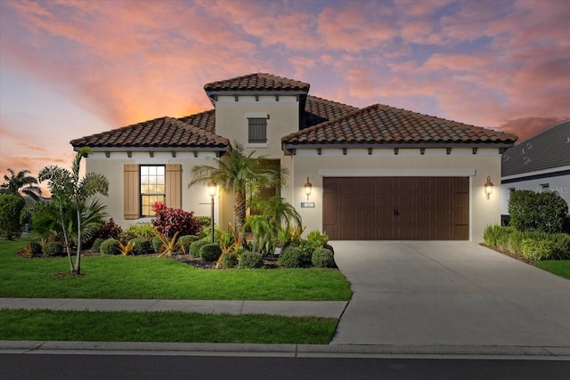 mediterranean / spanish-style house with a garage, driveway, a front lawn, and stucco siding