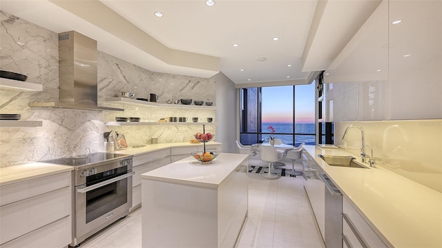 kitchen featuring tasteful backsplash, wall chimney exhaust hood, modern cabinets, appliances with stainless steel finishes, and a sink